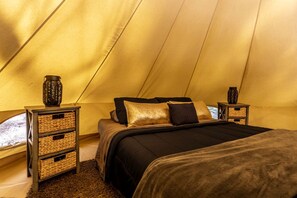 Una habitación con tienda de campaña, cama, dos mesitas de noche, cestas de mimbre y jarrones decorativos.