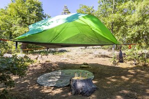 A green tent set up in a forested area with a table and chairs underneath.