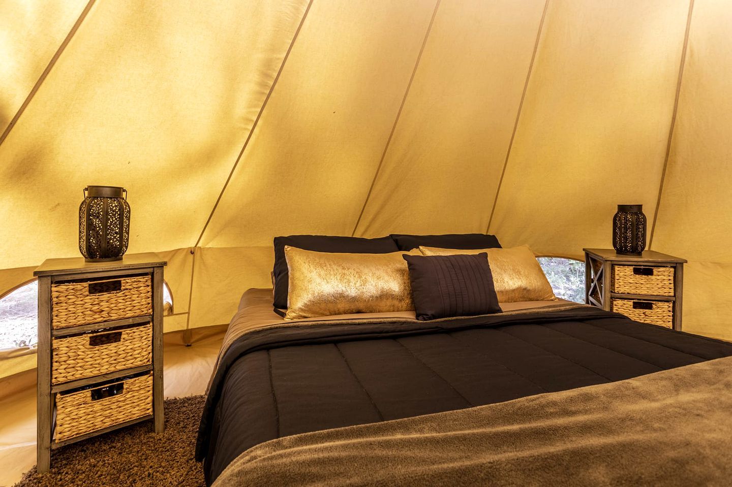 A tented room with a bed, two nightstands, and woven baskets.