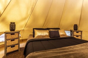 A tented room with a bed, two nightstands, and woven baskets.