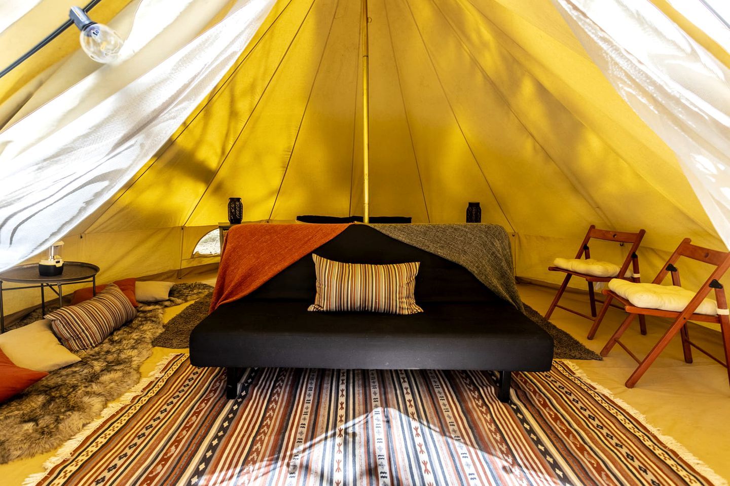 A tent with a bed, chairs, a table, and a lamp.