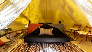 A tent with a bed, chairs, a table, and a lamp.