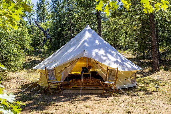 A tent with a triangular roof, two chairs, and a table in a forest.