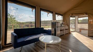 A tented accommodation with a sofa, a small round table, a refrigerator, and a view of the outdoors.