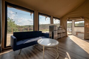 A tented accommodation with a sofa, a small round table, a refrigerator, and a view of the outdoors.