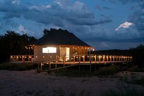 A beachside cabin with a deck and a covered porch, surrounded by natural landscape.