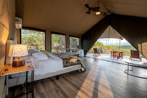 A bedroom with a bed, bedside table, lamp, and a view of the outdoors.