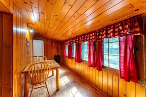 L’intérieur d’un chalet en bois, avec une table à manger, des chaises et une fenêtre ornée de rideaux rouges.
