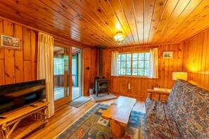 L’intérieur d’un chalet en bois, avec une télévision, un canapé, une cheminée et de grandes fenêtres.