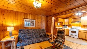 A wooden cabin interior with a sofa, a dining table, a kitchen area, and a ceiling light fixture. - Charming Pet-Friendly Cabin in Ely, Ideal for Getaways to Nature in Minnesota (Ely)