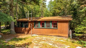 Eine rustikale Holzhütte mit einer Holzfassade, einem Schornstein und einem Fenster mit roten Vorhängen.