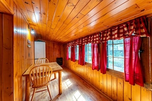 L’intérieur d’un chalet en bois, avec une table à manger, des chaises et une fenêtre ornée de rideaux rouges.