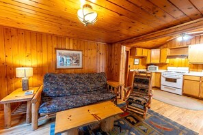 L’intérieur d’une cabane en bois, avec un canapé, une table à manger, un coin cuisine et un luminaire au plafond.