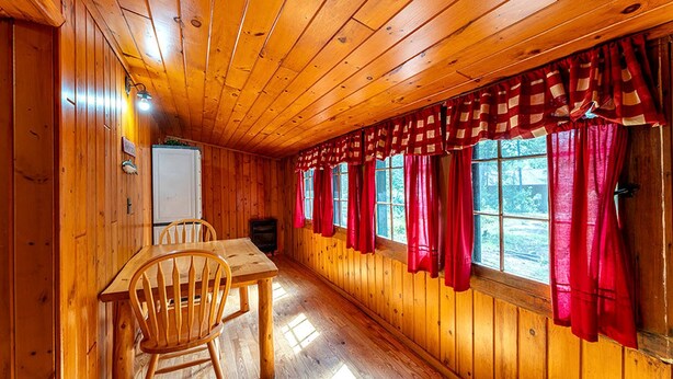 A wooden cabin interior with a dining table, chairs, and a window with red curtains. - Charming Pet-Friendly Cabin in Ely, Ideal for Getaways to Nature in Minnesota (Ely)