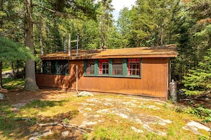 A rustic cabin with a wooden exterior, a chimney, and a window with red curtains. - Charming Pet-Friendly Cabin in Ely, Ideal for Getaways to Nature in Minnesota (Ely)