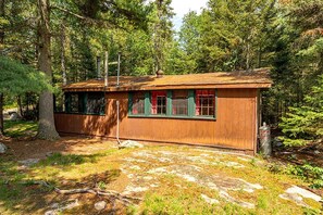 Une cabane rustique avec une façade en bois, une cheminée et une fenêtre ornée de rideaux rouges.