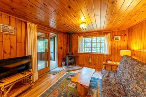 L’intérieur d’un chalet en bois, avec une télévision, un canapé, une cheminée et de grandes fenêtres.