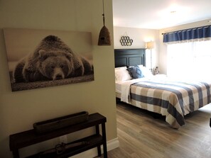 Ein Schlafzimmer mit einem Bett, einem Nachttisch, einer Wandlampe, einem Fenster mit Vorhängen und einem an der Wand befestigten Vogelhaus.