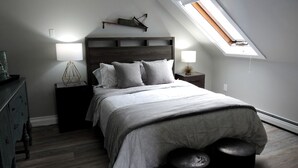 Un dormitorio con cama, mesitas de noche, cómoda, tragaluz y mesilla.