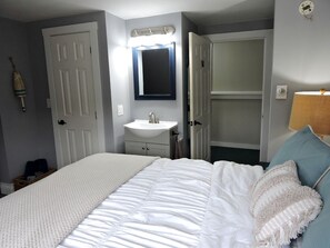 A bedroom with a bed, a bedside table, a nightstand, a wall-mounted mirror, and a closet. - Cabin Retreat for Nature and City Exploration near Sebago Lake State Park, ME (Casco)