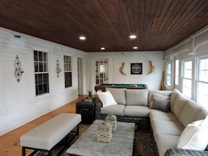 A cozy living room with a wooden ceiling, white walls, a pool table, and a sectional sofa. - Cabin Retreat for Nature and City Exploration near Sebago Lake State Park, ME (Casco)