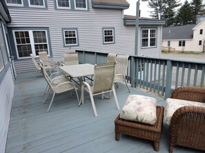 Une terrasse extérieure couverte, dotée d’une table et de chaises, d’un pouf en osier et d’une rambarde.