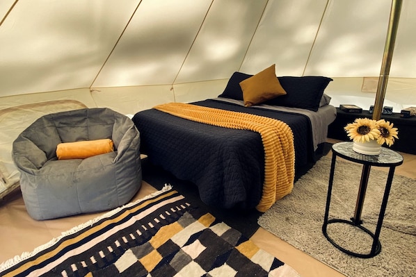 A tent-style room with a bed, a bean bag chair, a small table with a vase of sunflowers, and a patterned rug.