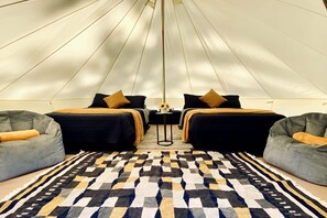 Una habitación tipo tienda de campaña con dos camas, un tapete estampado y dos sillones de mimbre.