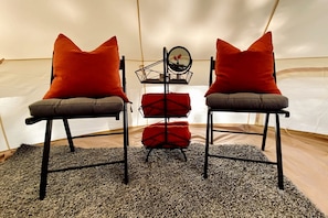 Dos sillas con cojines rojos, una mesita con un espejo y una alfombra gris en una habitación con forma de tienda.