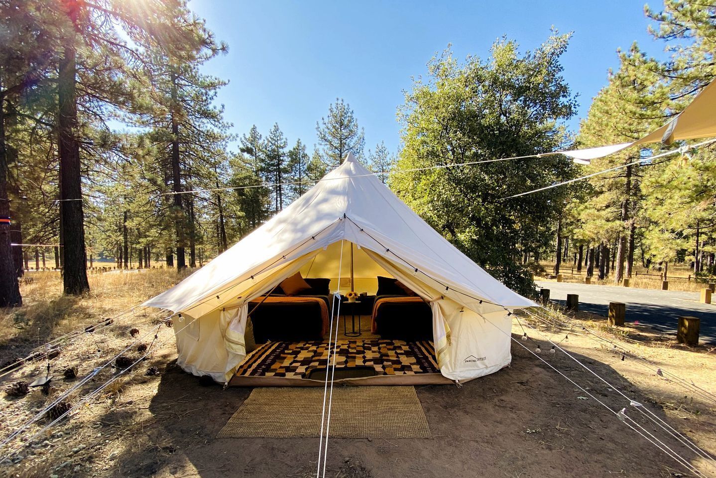 A tent with a checkered floor, a bed, and a table with a lamp.