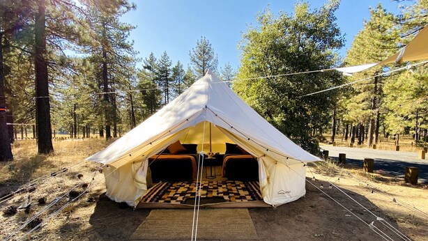 A tent with a checkered floor, a bed, and a table with a lamp.