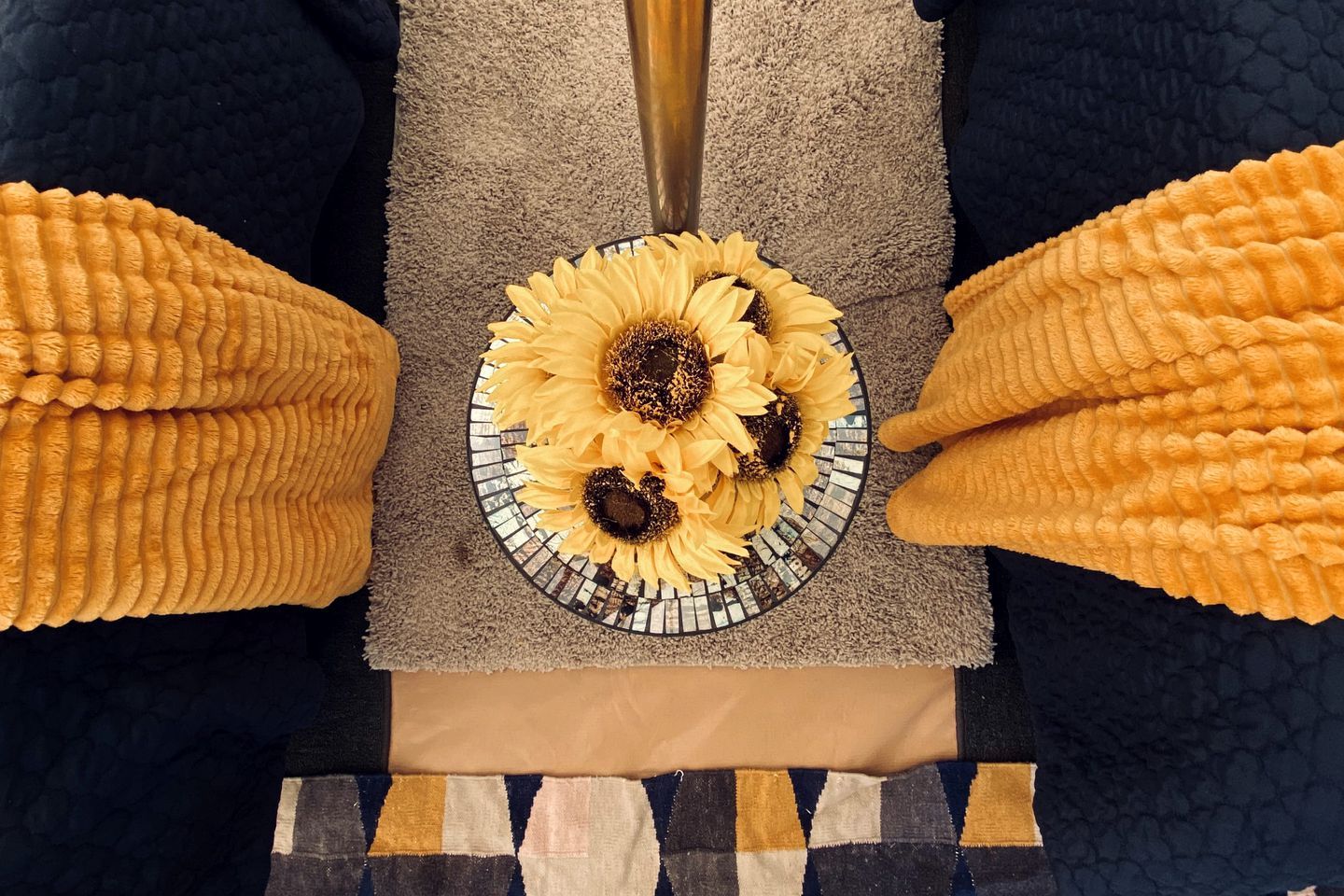 Una cama con una manta estampada, un plato decorativo con girasoles y un jarrón con flores.