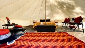 Interior de una tienda de campaña con una cama, zona de estar y una mesa con un jarrón.