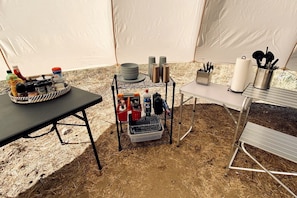 A tent with a dining table, a metal rack with condiments, and a metal table with utensils.