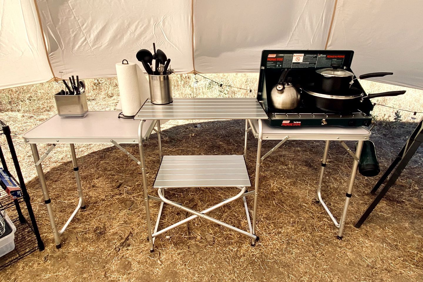 Ein tragbarer Propan-Kocher steht auf einem Metalltisch, darauf ein Topf, eine Rolle Küchenpapier und ein Besteckhalter.