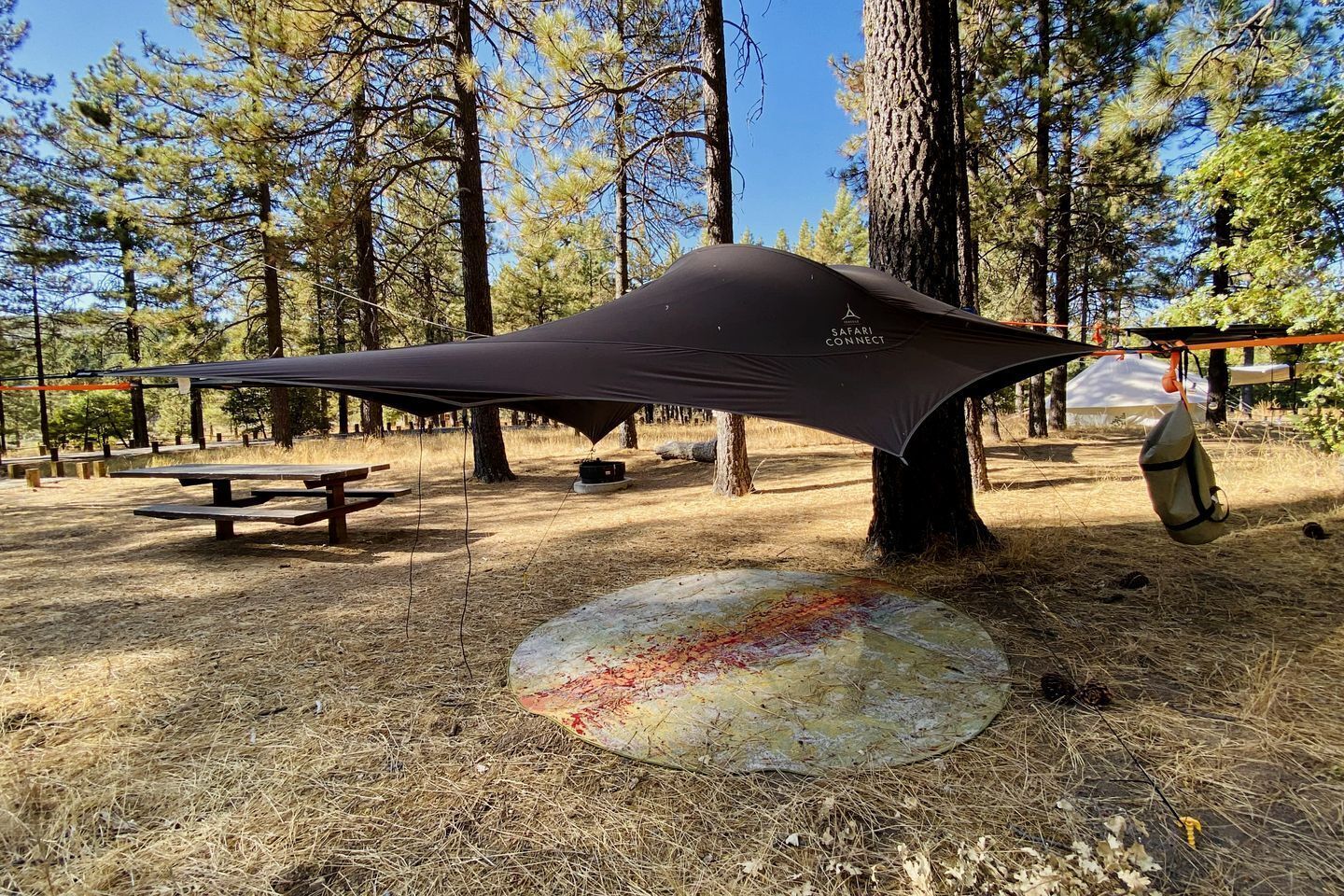 A camping area with a tarp shelter, picnic tables, and a fire pit.