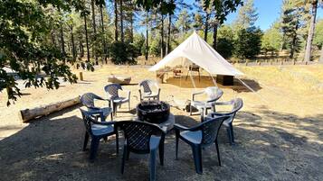 Een camping met een tent, een vuurkuil en plastic stoelen rondom een tafel.