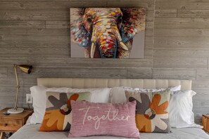 A bedroom with a wooden wall, a bed with multiple pillows, a bedside lamp, and a painting of an elephant. - Fully-Equipped Safari Tent Rental in Burnet for Luxury Glamping in Texas (Burnet)