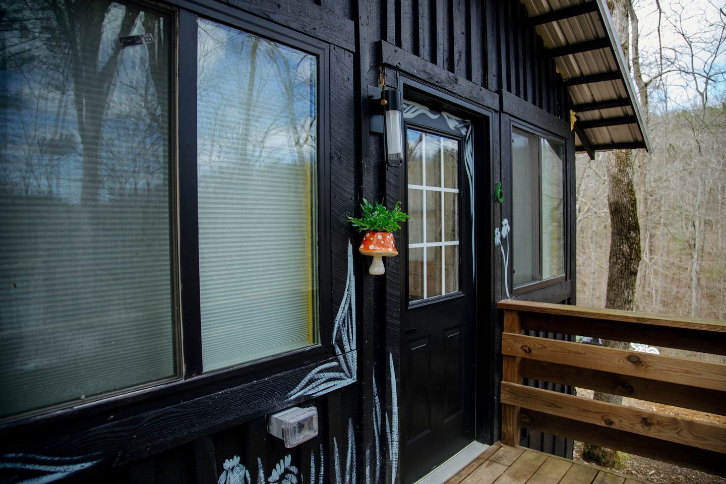 Une façade en bois avec une porte noire, de grandes fenêtres et une petite plante en pot placée près de la porte.