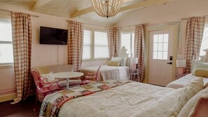 Un dormitorio con una cama, una silla, una mesita, un televisor y una puerta.