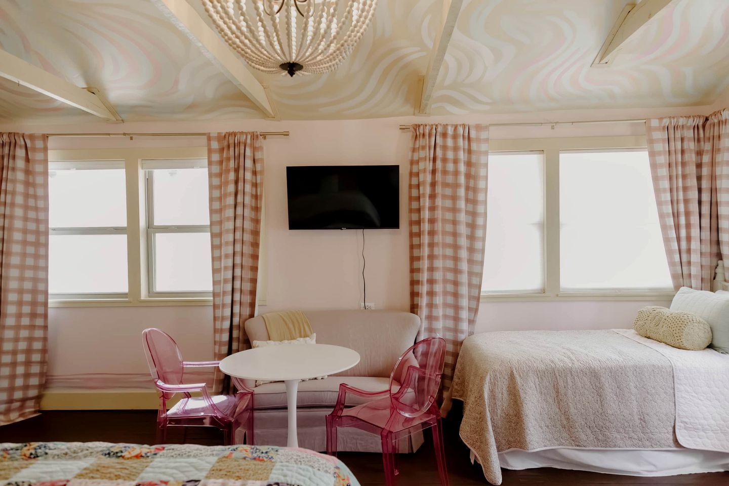 Une chambre avec un lit, une télévision, une table ronde avec des chaises et des rideaux à carreaux.