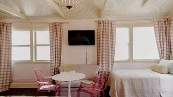Une chambre avec un lit, une télévision, une table ronde avec des chaises et des rideaux à carreaux.