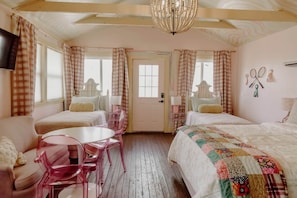 A room with two beds, a table, chairs, a chandelier, and a door.