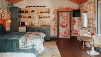 A bedroom with a bed, a desk, and a chair. There is a microwave and a cabinet.