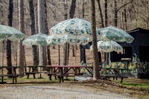 Eine Reihe von Picknicktischen mit gemusterten Sonnenschirmen, umgeben von Bäumen.