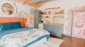 Un dormitorio con cama, un espejo redondo, una cocina con microondas y refrigerador.