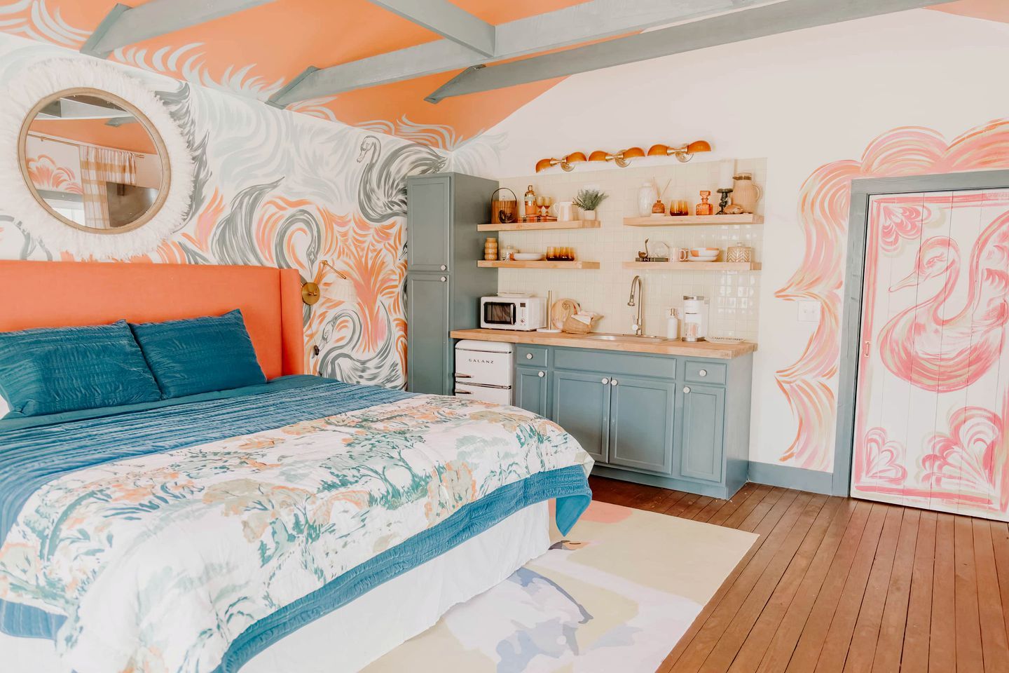Ein Schlafzimmer mit einem Bett, einem runden Spiegel, einer Küche mit einer Mikrowelle und einem Kühlschrank.