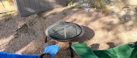 A covered outdoor seating area with a grill table, two folding chairs, and a storage unit.