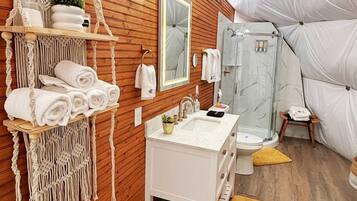 Ein modernes Badezimmer mit Holzvertäfelung, einem weißen Waschtisch, einem großen Spiegel, einer Dusche und einem Wandbehang aus Makramee.