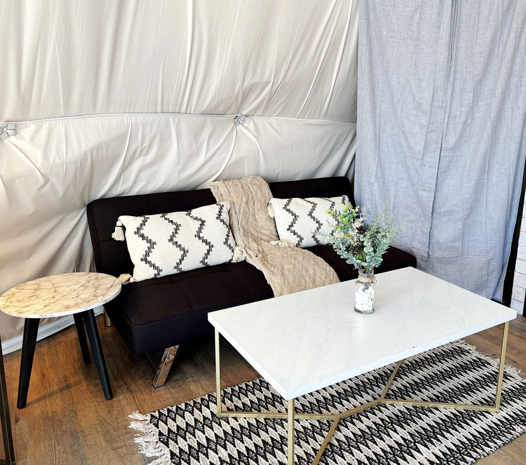 Ein Zimmer mit einem dunkelbraunen Sofa, einem weißen Tisch und einem gemusterten Teppich.